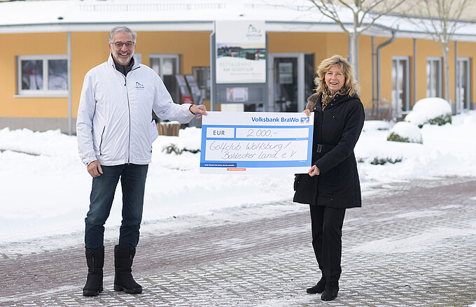 Norbert Preine, Präsident des Vorstandes des Golfclubs, nimmt die Spende symbolisch von Claudia Kayser, Leiterin der Direktion Wolfsburg der Volksbank BraWo, entgegen.