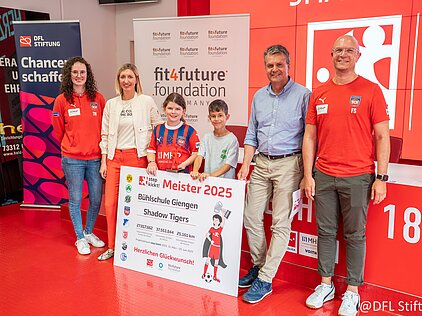 Gruppe vor Sponsor-Bannern mit Kindern, die ein "Meister 2025"-Schild halten, während einer Preisverleihung.