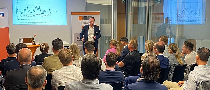 Der Referent Ansgar Nolte steht im Hintergrund des Bildes und referiert. Im Vordergrund sind die anwesenden Gäste sitzend von hinten fotografiert. 
