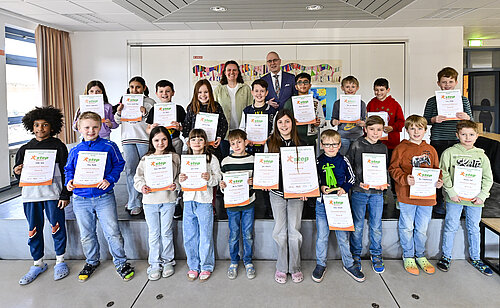 Eine Gruppe von Kindern steht aufgereiht und strahlend mit Urkunden in den Händen in einem hellen Raum.