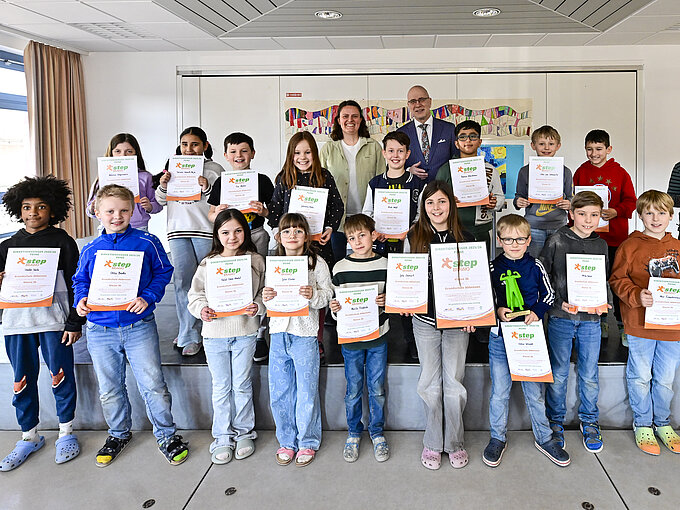 Eine Gruppe von Kindern steht aufgereiht und strahlend mit Urkunden in den Händen in einem hellen Raum.