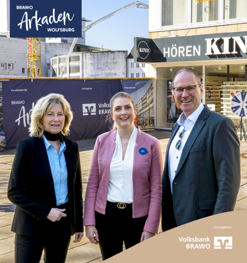 Drei Personen stehen vor den Brawo Arkaden in Wolfsburg, lächelnd in die Kamera, mit Bauarbeiten im Hintergrund.