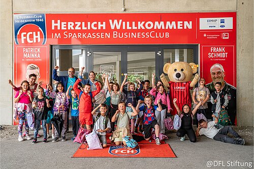 Kindergruppe jubelt mit Maskottchen vor dem Sparkassen BusinessClub des FC Heidenheim.