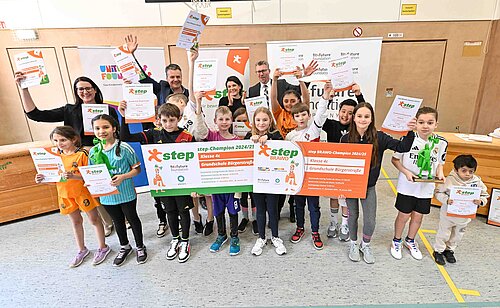 Kinder und Erwachsene halten stolz Urkunden und Plakate in einer Sporthalle hoch.