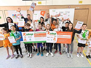 Kinder und Erwachsene halten stolz Urkunden und Plakate in einer Sporthalle hoch.