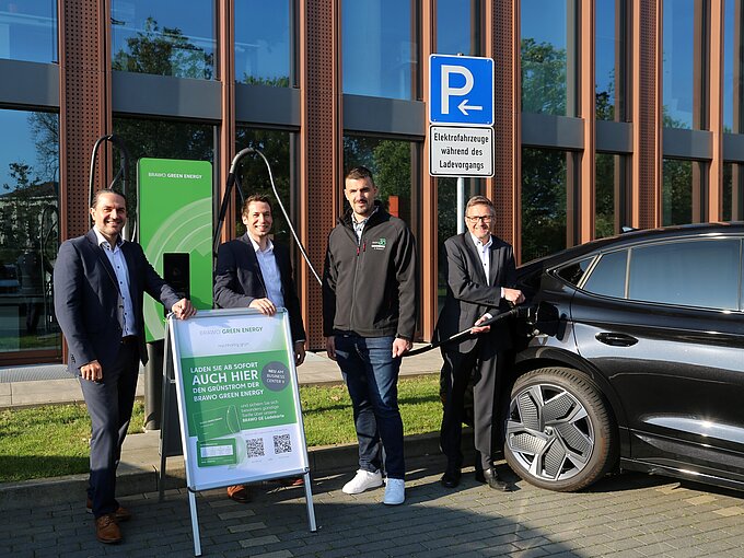 Vier Männer neben einem Elektroauto an einer Schnelladesäule mit einem BRAWO Green Energy Schild am Business Center II des BraWoParks.