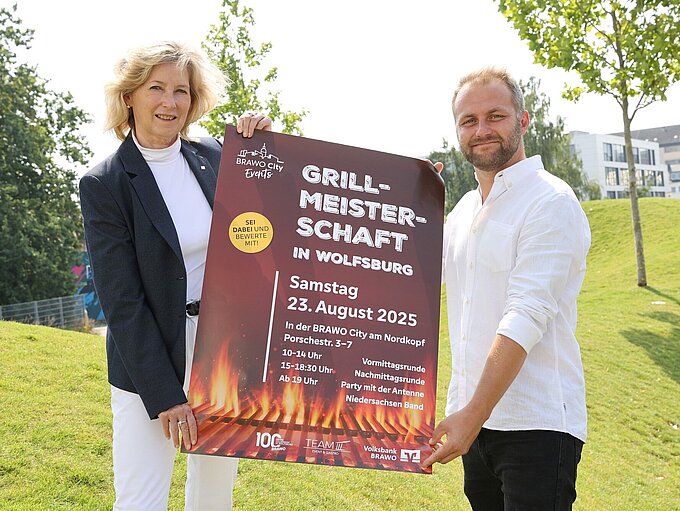 Zwei Personen stehen und halten ein Plakat fest zur Ankündigung der Veranstaltung.