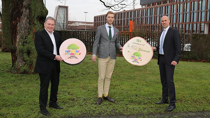 Janis Meyerhof (Mitte) von den Niedersächsischen Landesforsten nimmt die 4.182 Bäume symbolisch von André Bonitzke (r.), Leitung Privatkunden der Volksbank BraWo, im Beisein von Thomas Fast entgegen.