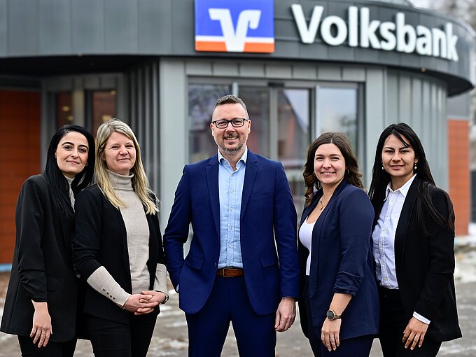 Fünf Personen in Businesskleidung vor einem Volksbank-Gebäude lächeln in die Kamera.