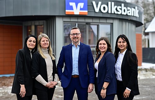 Fünf Personen in Businesskleidung vor einem Volksbank-Gebäude lächeln in die Kamera.