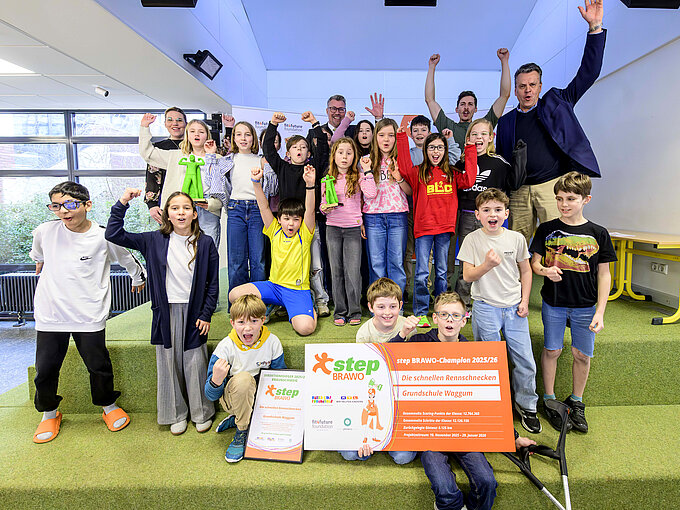 Eine Gruppe von Kindern und Erwachsenen jubelt mit Urkunden und step-BRAWO Pokalen in der Hand.