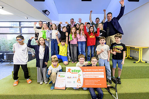 Eine Gruppe von Kindern und Erwachsenen jubelt mit Urkunden und step-BRAWO Pokalen in der Hand.