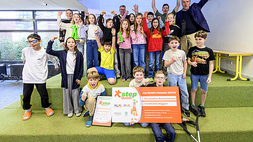 Eine Gruppe von Kindern und Erwachsenen jubelt mit Urkunden und step-BRAWO Pokalen in der Hand.